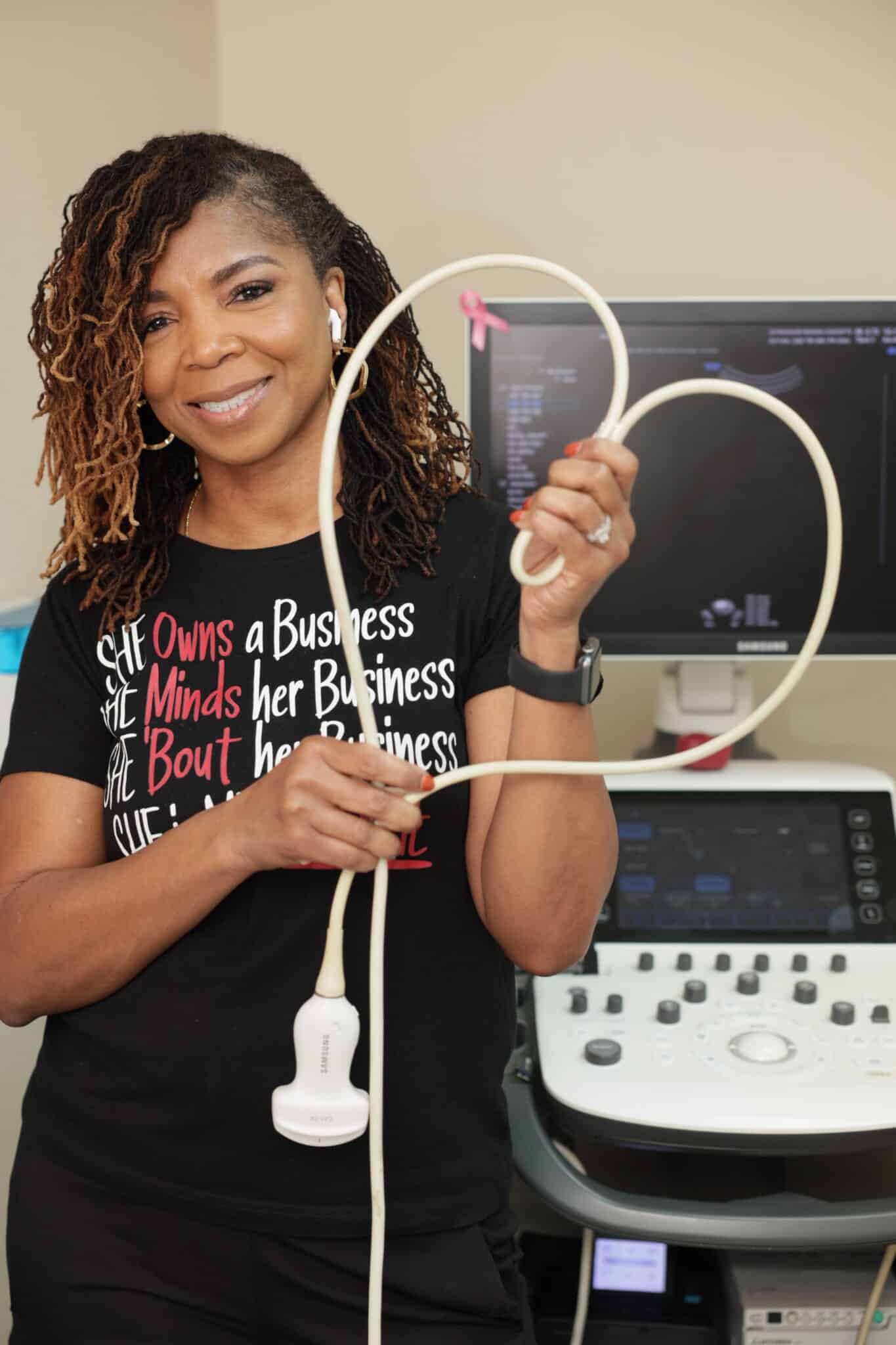 Ultrasound business owner holding probe cord shaped like a heart in front of ultrasound machine