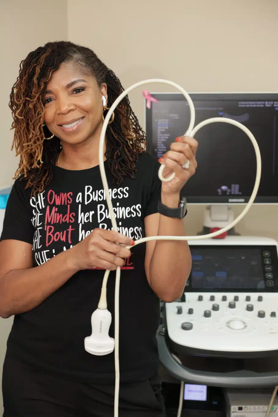 Ultrasound business owner holding probe cord shaped like a heart in front of ultrasound machine